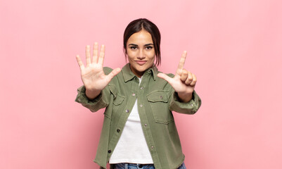 pretty young woman smiling and looking friendly, showing number seven or seventh with hand forward, counting down