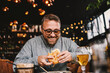 © dusanpetkovic1 - Middle aged bearded hungry man sitting in restaurant and eating delicious burger.