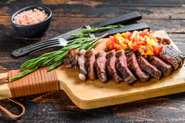 Grilled top sirloin cap or picanha steak on a cutting board with herbs. Dark wooden background. Top view