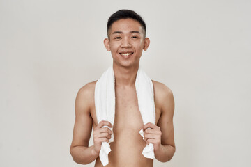 Portrait of shirtless young asian man with problematic skin and hyperpigmentation on his face posing with towel around his neck isolated over white background