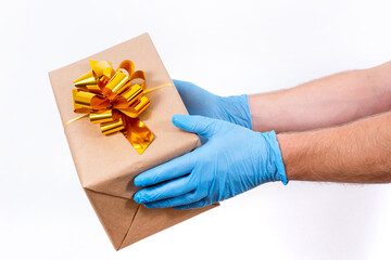 Safe contactless remote delivery of holiday gifts during the coronavirus pandemic. Close up. Courier hand in protective medical gloves holds a beautiful gift box with a bow on a white background