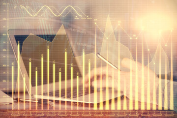 Double exposure of man's hands holding and using a digital device and forex graph drawing. Financial market concept.