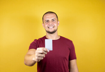 Russian man wearing basic red t-shirt over yellow insolated background showing a white card.