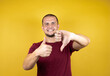 © Irene - Russian man wearing basic red t-shirt over yellow insolated background Doing thumbs up and down, disagreement and agreement expression. Crazy conflict