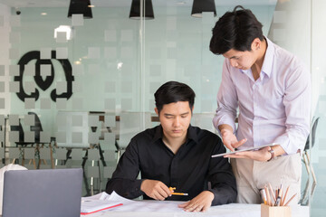 Cropped shot of two engineers working together with blueprint, laptop and tablet on white desk