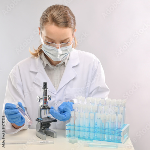 Doctor in protective clothing looks in microscope and exploring covid-19 vaccine on biological tubes background. Backstage of scientific discovery. Healthcare and coronavirus infection concept.