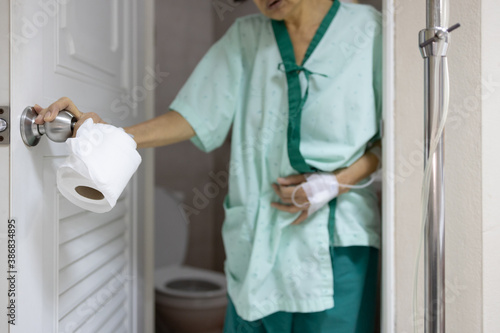 Sick asian senior woman with diarrhea,food poisoning hold tissue roll,opening the toilet door,elderly people have abdominal pain,stomach ache,symptom of irritable bowel syndrome or colorectal cancer.
