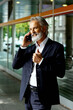 Portrait of a smiling senior man talking on phone in business jacket in front of glass building in the city
