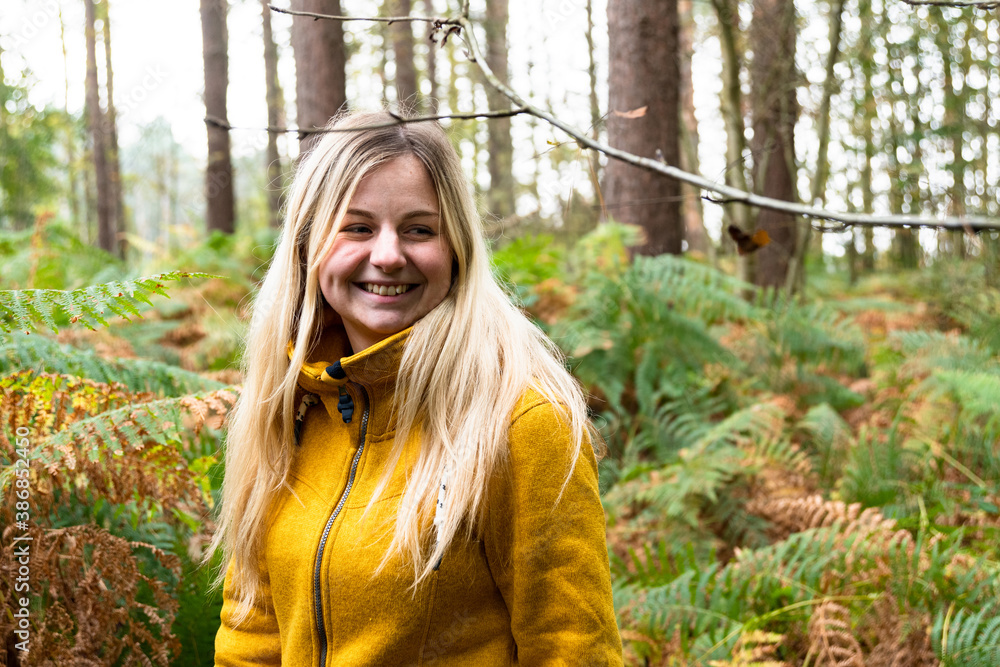 Blonde woman in yellow jacket walking through a forest clearing ...