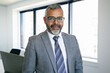 © Mangostar - Content Indian CEO standing and smiling for portrait. Successful pensive bearded businessman in glasses posing in office room and looking at camera. Business, expression and management concept