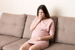 © sosiukin - Young vomiting woman sitting on sofa and suffering with nausea. Pregnancy expectation concept, copy space