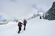 © anatoliy_gleb - Male travelers with backpacks walking uphill in winter mountains. Group of alpinists with trekking sticks walking through snow and heading to mountaintop. Concept of hiking and mountaineering.