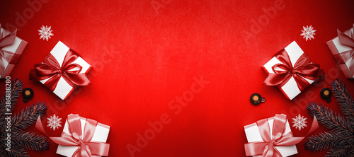 Xmas background red. White gift box with scarlet ribbon, New Year balls and sparkling lights in Christmas composition on dark red background for greeting card. Xmas backdrop with space for text.