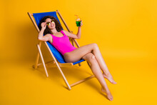 Photo Portrait Of Curly Brunette Girl Lying Sunbathing In Deckchair Drinking Holding Cocktail In Hand Touching Glasses Wearing Pink Swim Wear Isolated On Vivid Yellow Colored Background