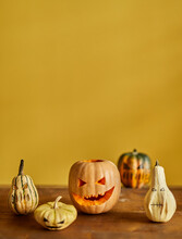 Jack O' Lantern On A Wood Table With Other Four Pumpkins Yellow Background Vertical
