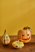 Jack O' Lantern On A Wood Table With Other Four Pumpkins Yellow Background Vertical Shot Diagonal Perspective