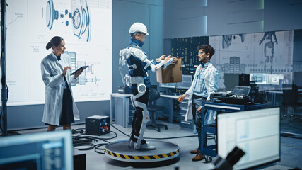 Poster - In Development Laboratory: Engineers Work on a Robotic Exoskeleton with a Person Testing it by Holding Heavy Cardboard Box. Designing Wearable Exosuit to Help Hard Labor Warehouse Workers
