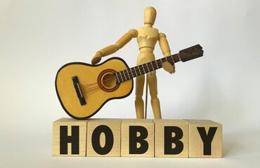 Wooden man holding a guitar, wooden cubes with the inscription hobby.Photo on a white background.The concept of a hobby.