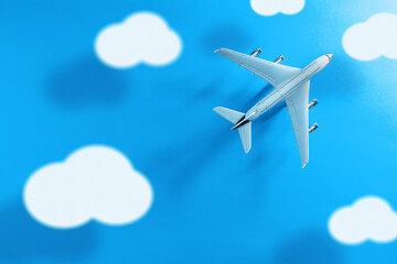 Top view of a commercial plane with clouds and long shadow on a blue background.