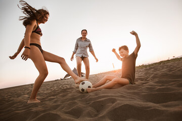 Happy family playing football on the beach having great family time on summer holidays.