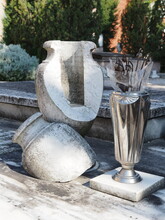 Ferrara, Italy. Certosa Monumental Cemetery. Old Broken Stone Vase, Next To It Is A Modern Metal Vase.
