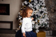 © lialia699 - Happy smiling mixed girl with dark hair sitting on the carpet. Christmas tree in the background.