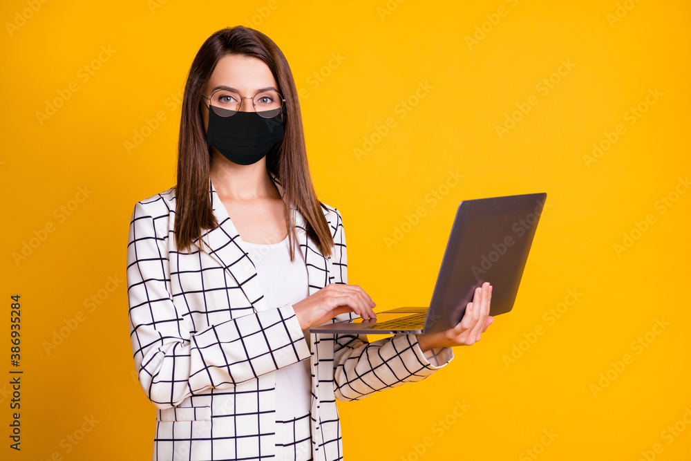 Photo portrait of pretty woman keeping laptop wearing black face mask smiling isolated on bright yellow color background - obrazy, fototapety, plakaty 