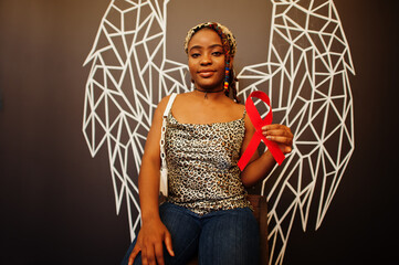 Wall Mural - AIDS awareness. Stylish african american woman hold red ribbon against wall with wings.