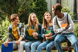 © LIGHTFIELD STUDIOS - Smiling teenagers with books looking at african american friend on bench outdoors
