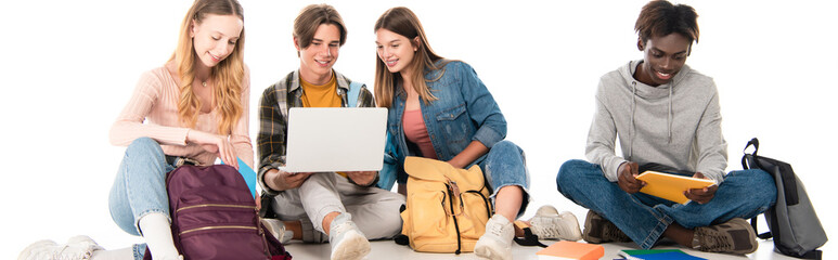 Website header of smiling multiethnic teenagers looking at laptop near books and backpacks on white background