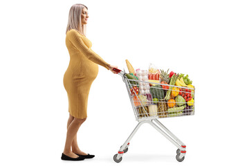 Wall Mural - Full length profile shot of a pregnant woman pushing a shopping cart with food