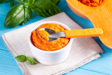 Pumpkin and carrot baby puree in bowl with baby spoon on blue background