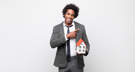 Wall Mural - young black afro man smiling cheerfully, feeling happy and pointing to the side and upwards, showing object in copy space