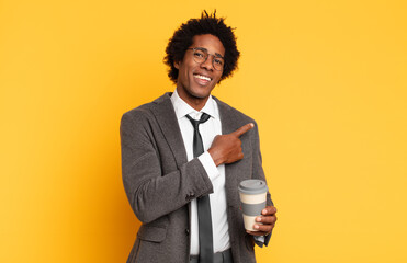 Wall Mural - young black afro man smiling cheerfully, feeling happy and pointing to the side and upwards, showing object in copy space