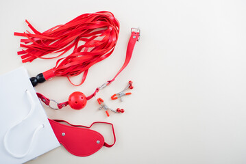 Top view of a red bdsm set in a white paper bag on a white background. Flat lay from sex toys