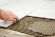 © fotoduets - Worker hands gluing white ceramic tiles on floor. Closeup.