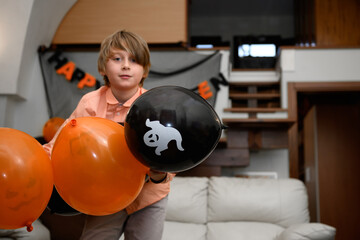 a boy is having fun and playing with orange and black Halloween baloons. Children get ready for celebrate Halloween at home, decorate home