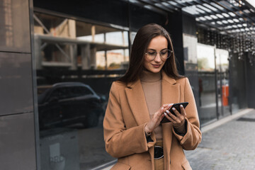 Wall Mural - Portrait of a beautiful caucasian businesswoman standing near the office and typing on her cell phone.