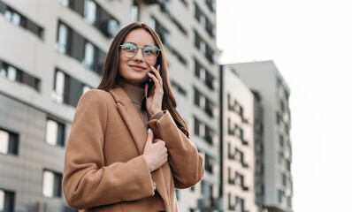 Wall Mural - Happy pretty brunette girl using mobile phone near office, beautiful woman browsing phone and doing online shopping in a mobile app while smiling walking near shopping mall.