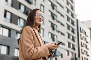 Wall Mural - Business Woman walking down the city street and talking on mobile phone. Female business professional walking outside with an office building in background.