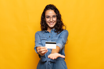 young hispanic woman smiling happily with friendly, confident, positive look, offering and showing an object or concept