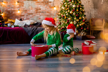 Wall Mural - Two young children in pajamas and Santa hats unpack Christmas presents in the room