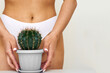The girl holds a large cactus in the groin or bikini area. The concept of intimate hygiene, epilation and depilation, deep bikini shaving