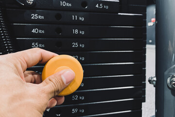 Young athlete hand change weight on iron heavy plates stacked of weight machine in gym and fitness center.