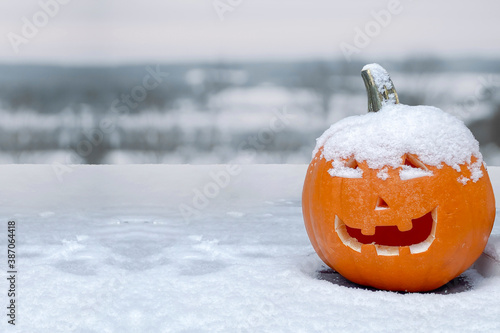A jack-o\'-lantern carved pumpkin during a snow fall during the fall. Concept: cold halloween. Snow fall during halloween