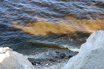 waves run onto the shore and crash against the rocks, creating many splashes and splashes near the shore. river surf in stormy weather near a stone pebble coast with foamy splashing waves.