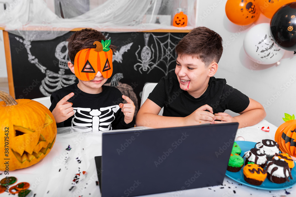 Happy young boys, brothers talking with grandparents via video call using laptop on halloween day , excited kid showing his new mask for halloween on camera - obrazy, fototapety, plakaty 