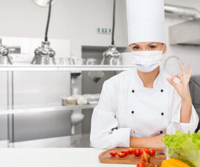 Sticker - cooking, culinary and health concept - female chef in toque wearing face protective mask for protection from virus disease with food on table showing ok hand sign over restaurant kitchen background