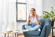 © Syda Productions - people, technology and leisure concept - happy young african american woman in headphones sitting in chair and listening to music at home