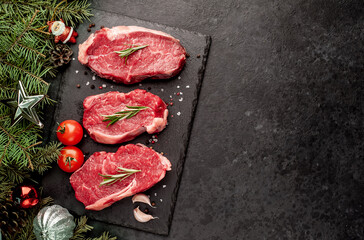 Three raw beef steaks with spices for Christmas with toys and a Christmas tree on a stone background with copy space